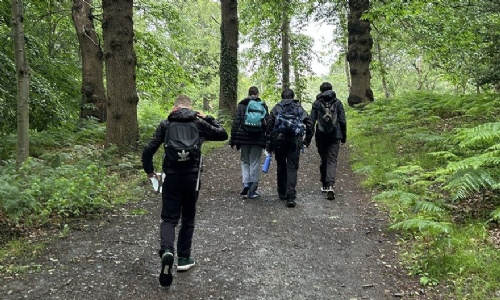 Group of four students with ruck sacks on walking through a forest